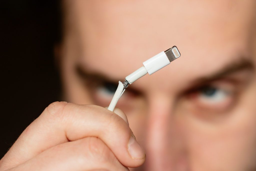 Angry man looking at his broken charger cable.