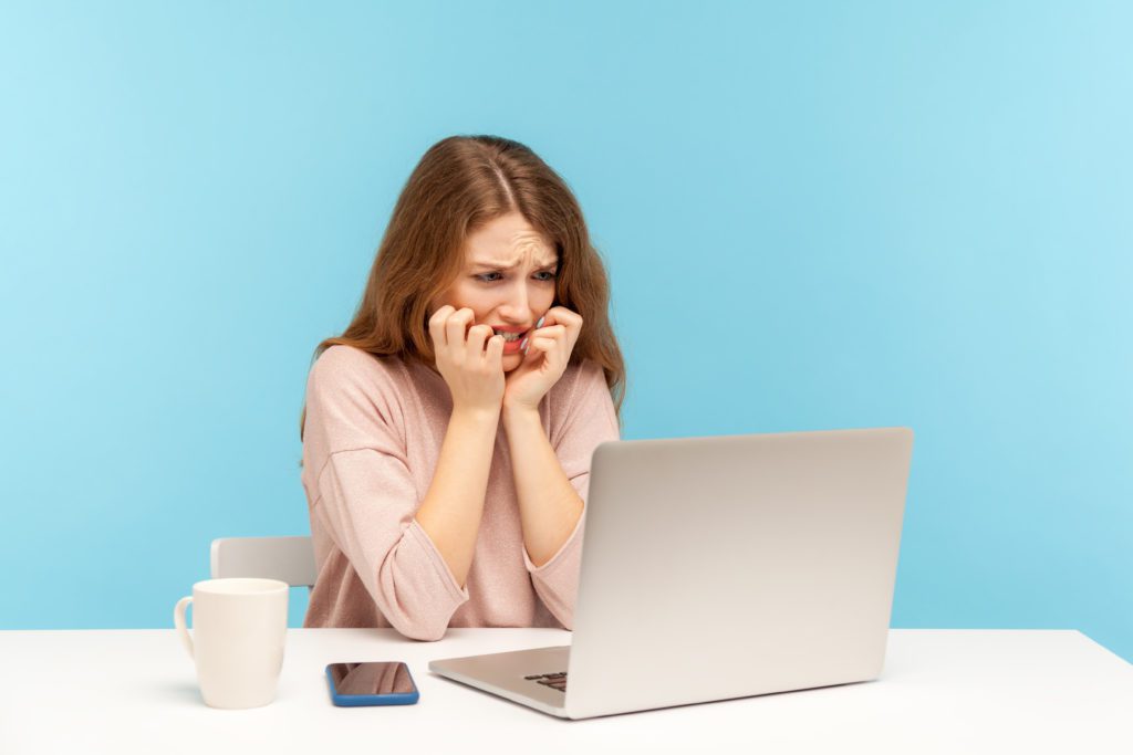 Anxious woman looking at her laptop, blue background.