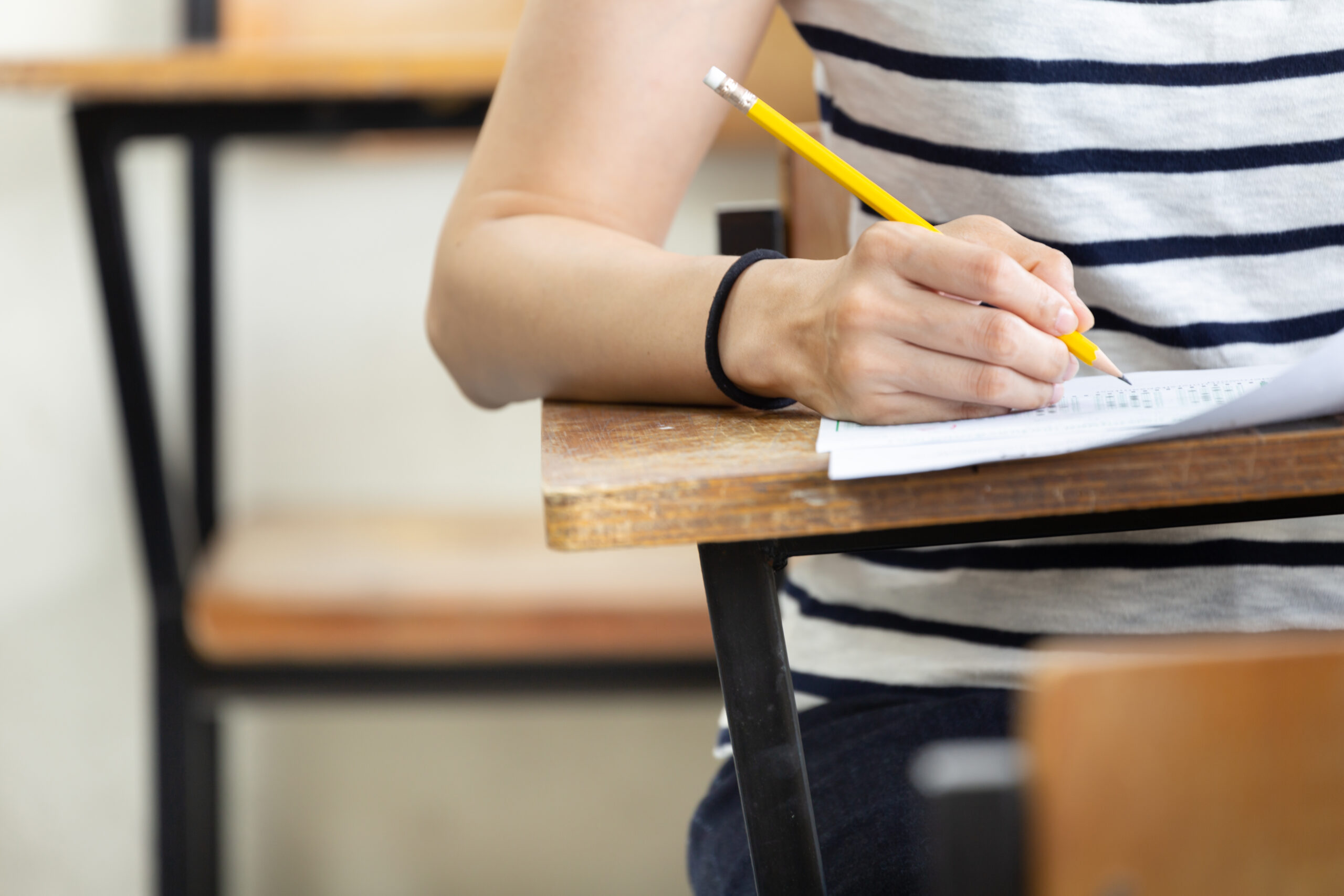 high school student holding pencil writing at her desk in the classroom