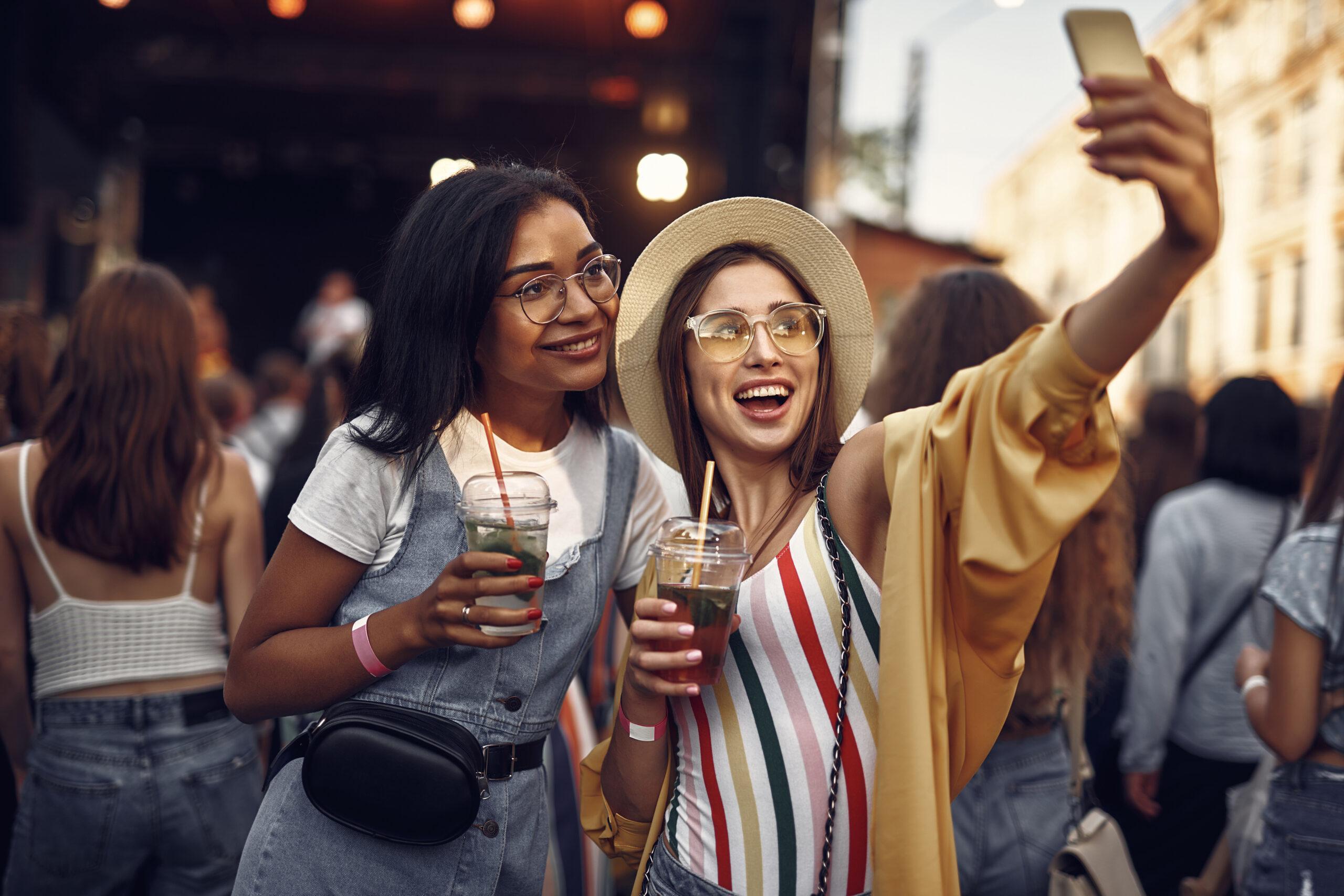 Two cheerful girls with cocktails making selfie