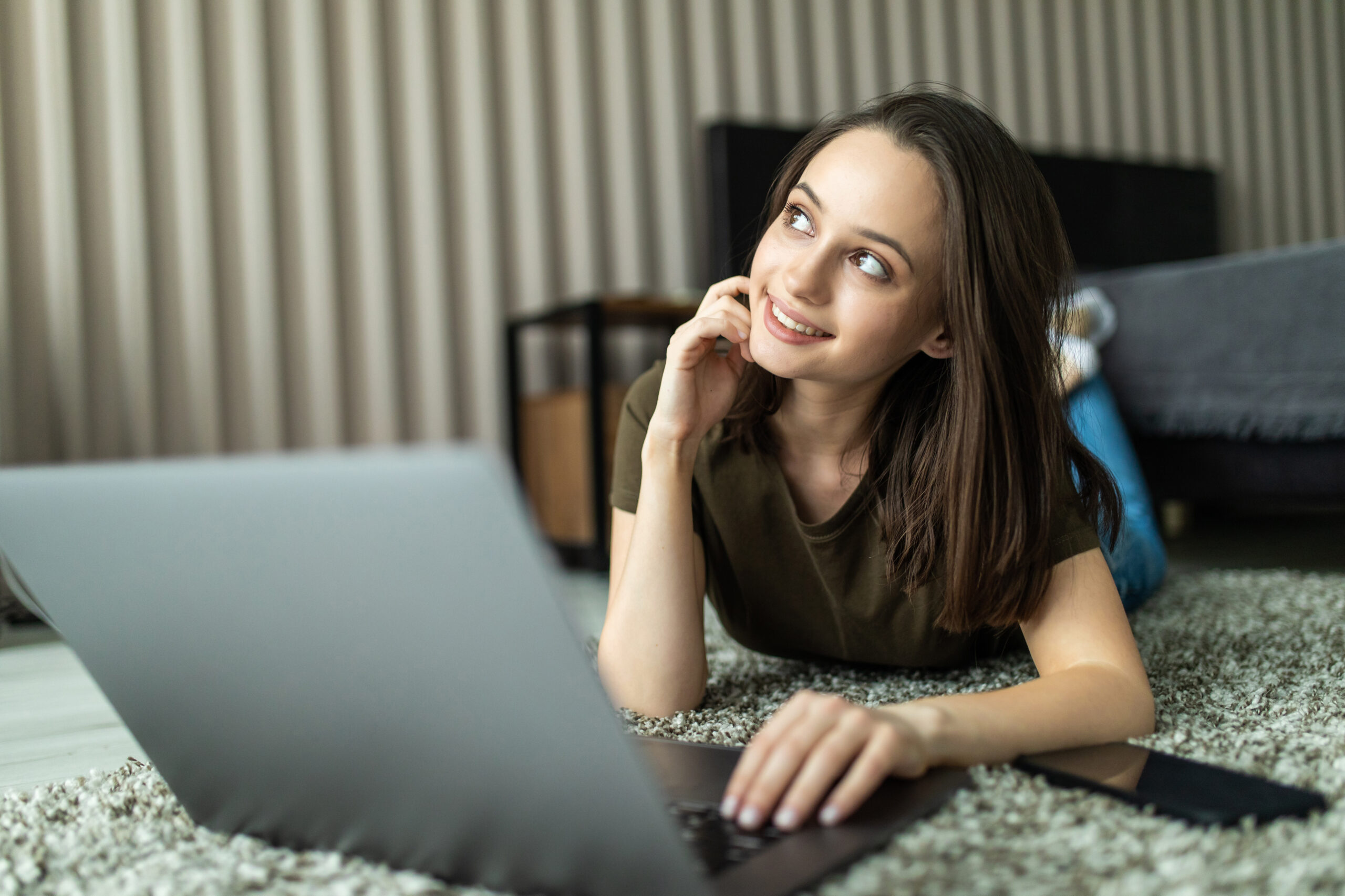 pensive young woman using laptop sitting on the floor with hand on chin