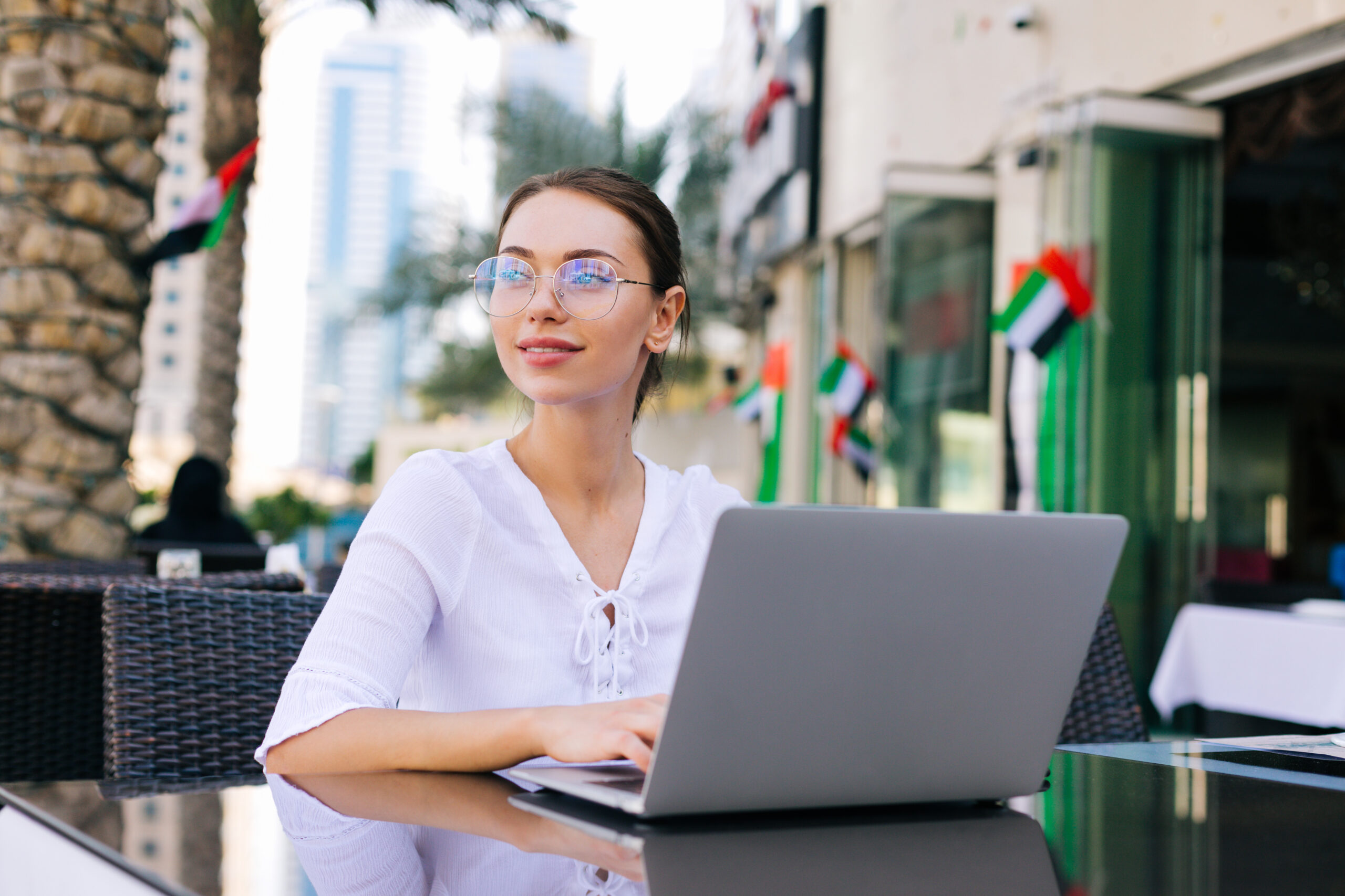 Young beautiful woman in eyeglasses working on laptop and sitting outdoors