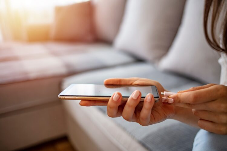 Female hand connecting charger to smart phone at home.