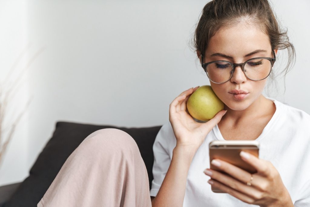 Woman using a cellphone and holding an apple.