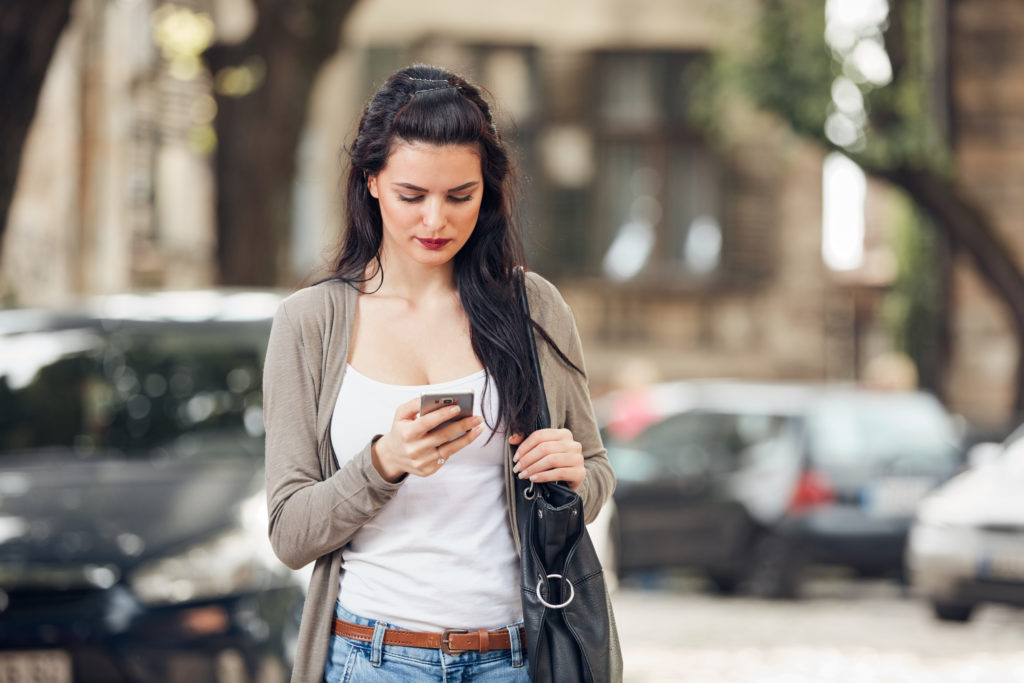 Pretty but serious looking young woman using smartphone on the street.
