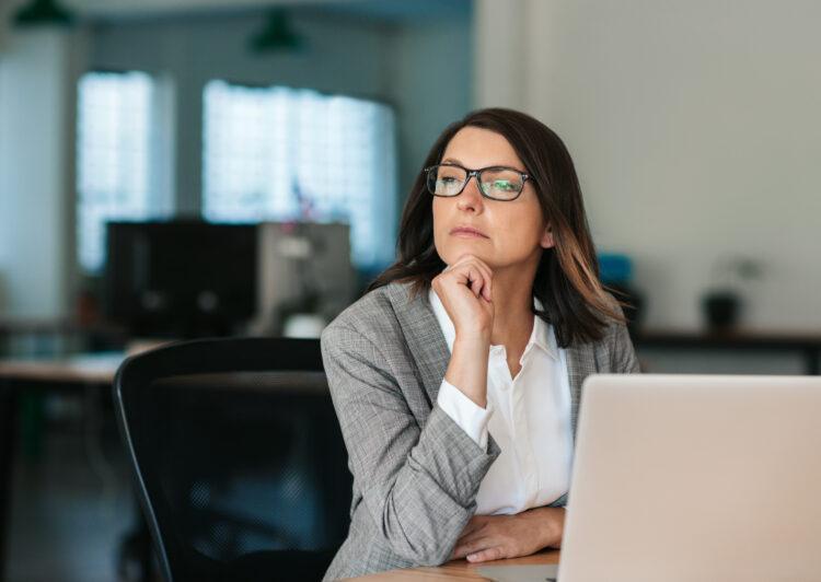 Serious professional woman thinking in front of laptop in office