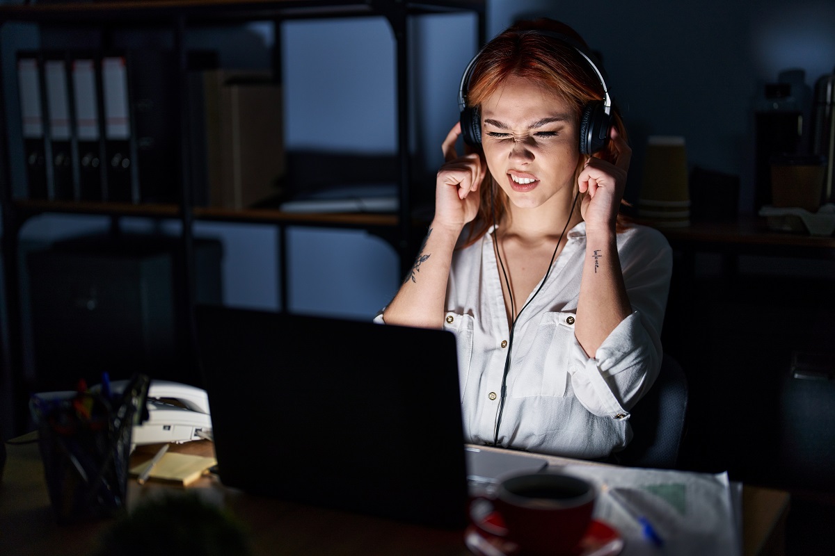 young woman using laptop cringing while listening in headset 