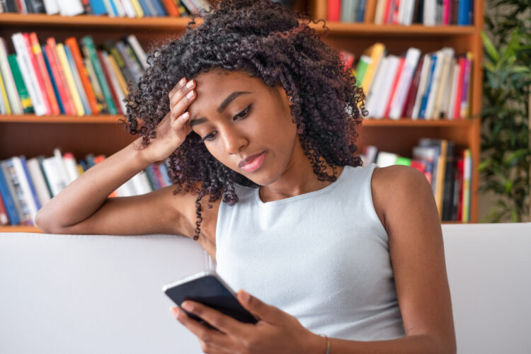 Upset black girl holding mobile phone at home