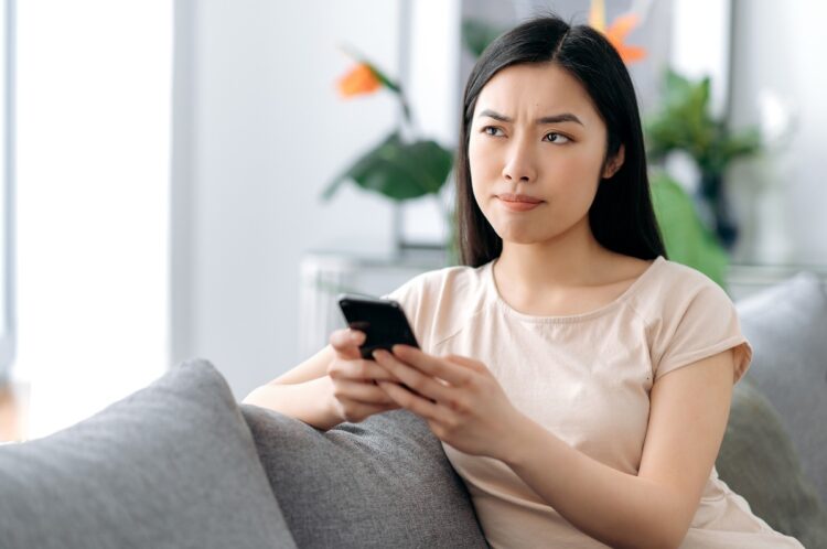A pensive cute woman holds her smartphone in her hand