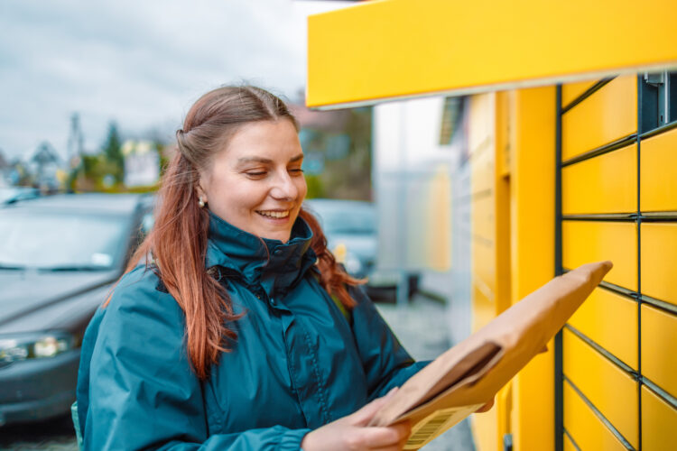 woman send or receive parcel with self service post terminal machine. 