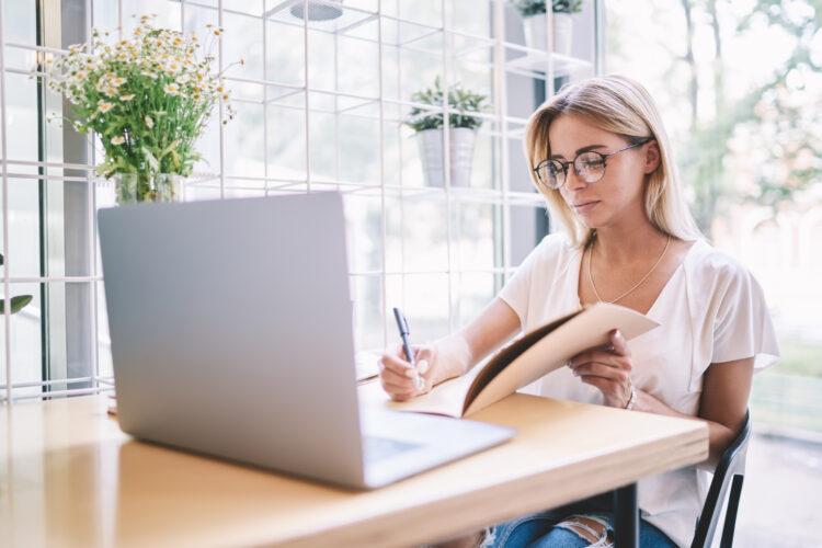 Focused female professional writing something in a document, with laptop on the table.
