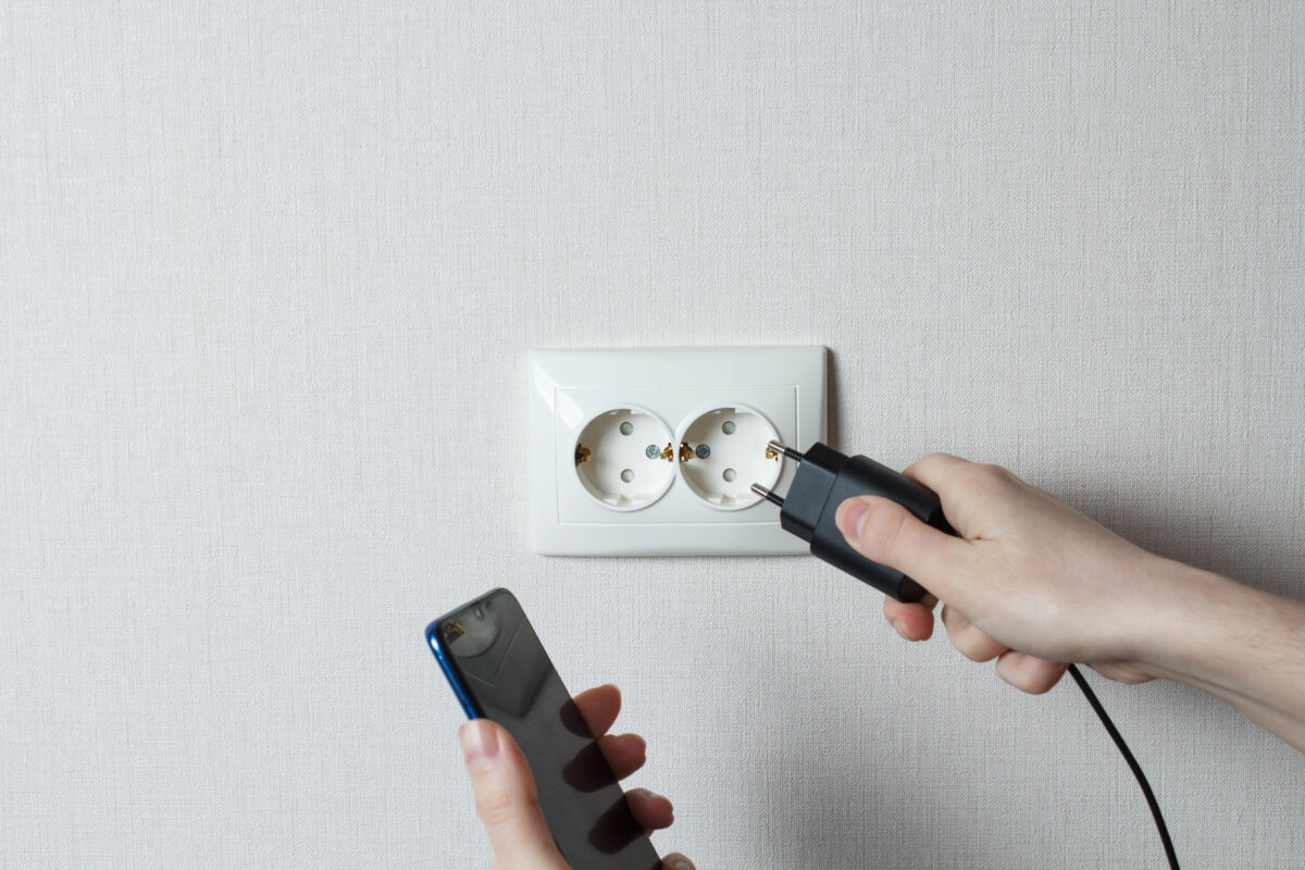 Young woman connects the mobile phone to the socket.