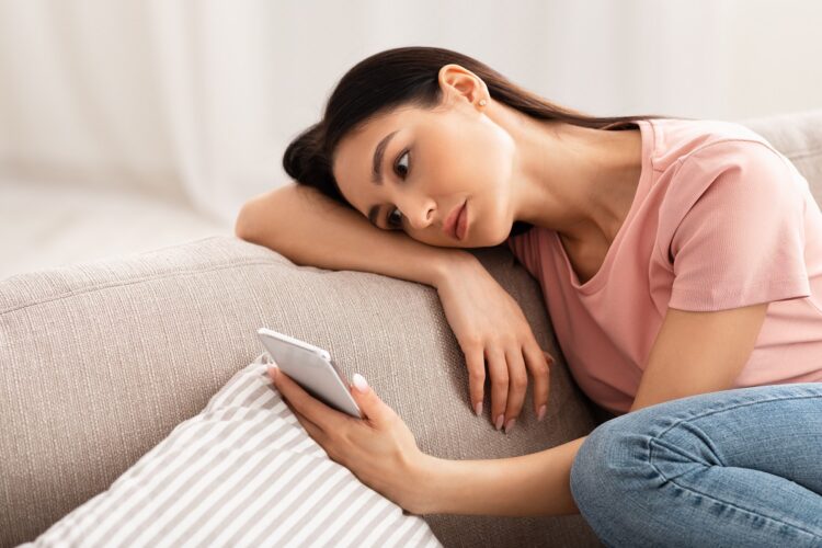 Frustrated woman checking mobile phone sitting on the couch