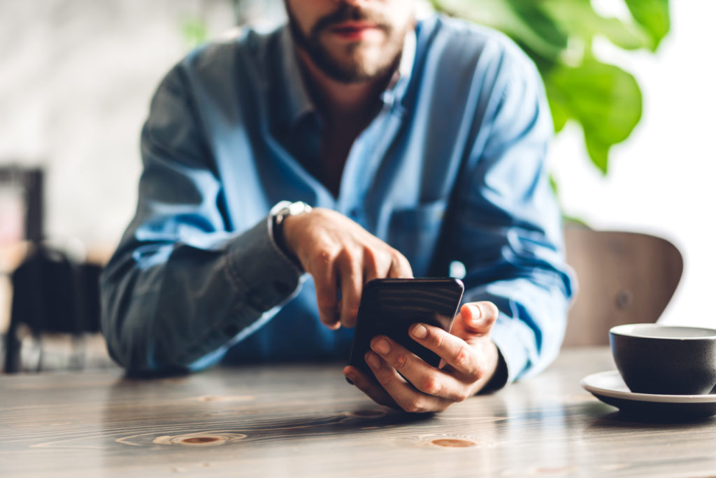 Handsome bearded man uses smartphone while having coffee.