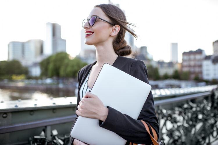 Professional woman walking on the street with a laptop.