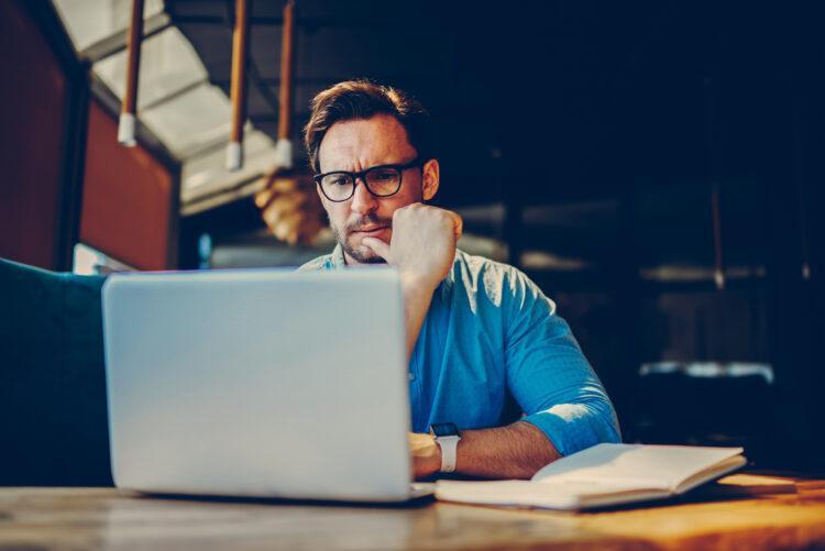 worried man with glasses looking at computer at desk