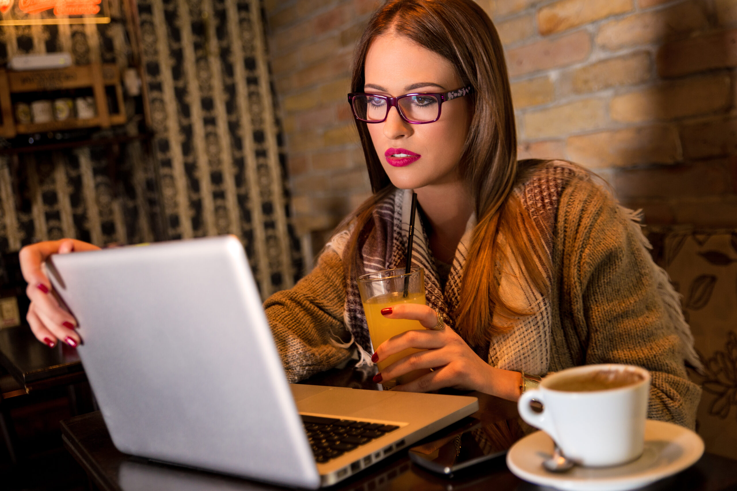 attractive young woman with glasses sitting in a cafe and working on her laptop