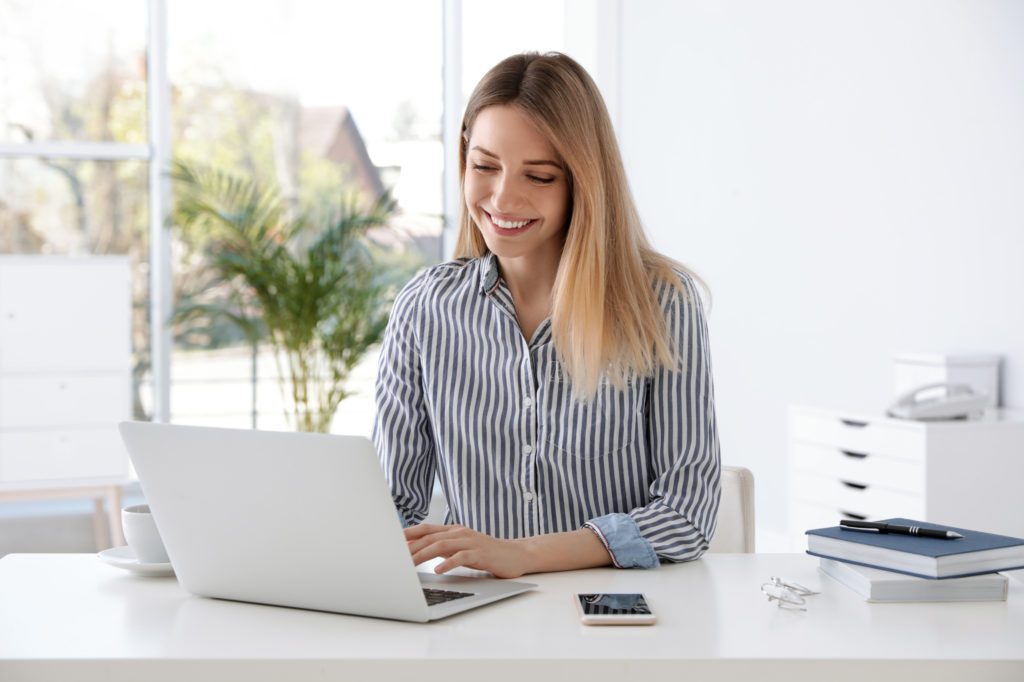 Businesswoman using her laptop inside a white colored office.