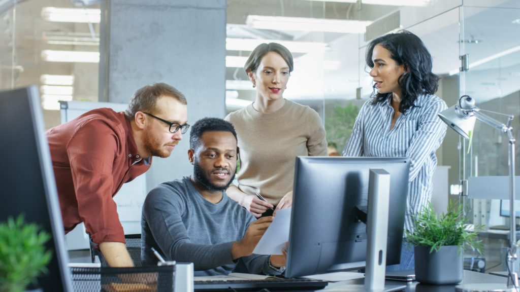 Busy corporate office with team helping their coworker on a problem.