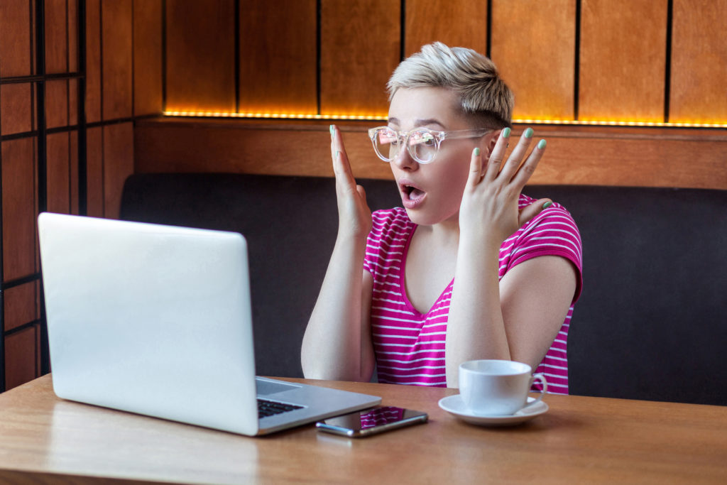 A woman with a shocked reaction while looking at her laptop.