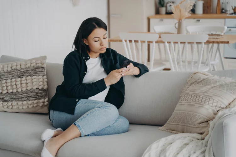 Young serious woman is looking at her phone sitting at the sofa