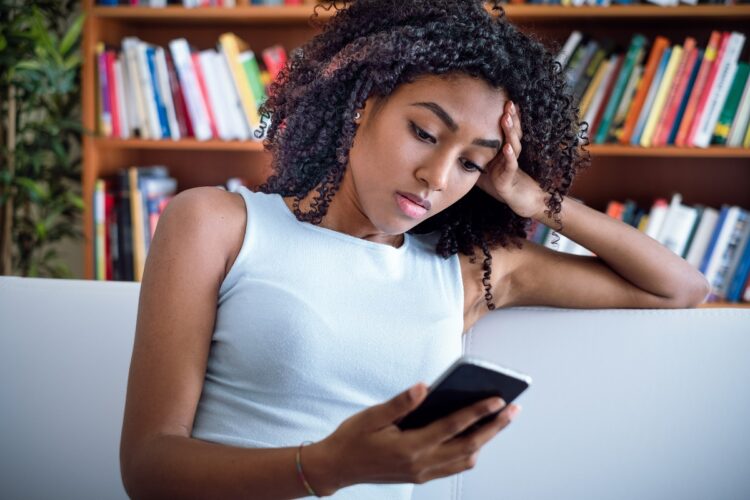 Sad woman lying on the couch at home feeling bad looking at cellphone