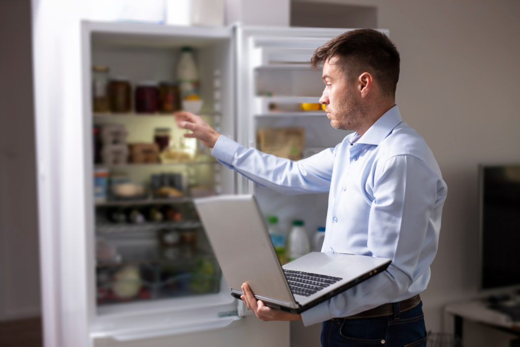 Man holding a laptop in front of refrigerator