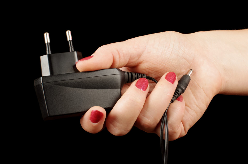 Female hand holding an AC charger adapter.
