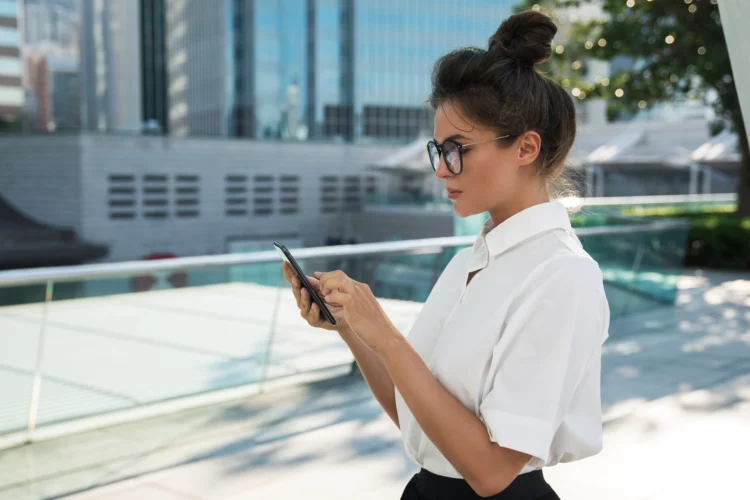 Young woman using her mobile phone in the city with modern buildings