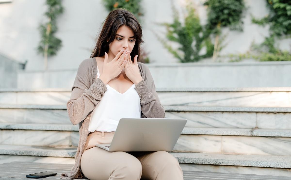 Woman with laptop shocked outdoors