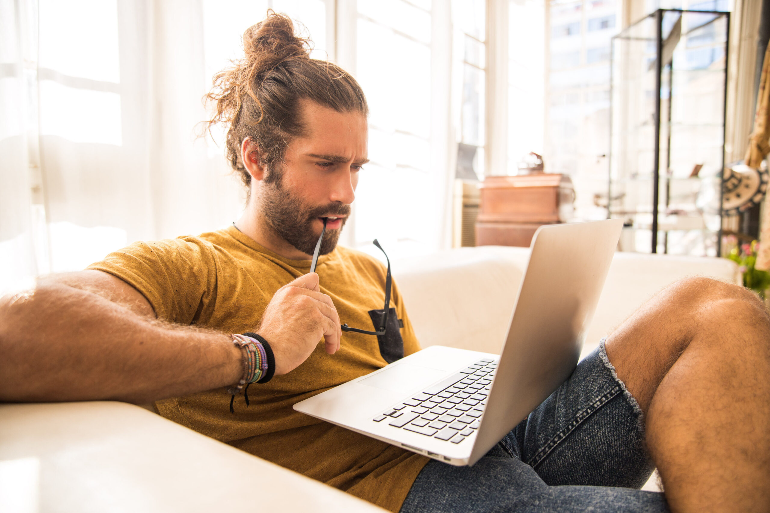 man with long hair sitting on a sofa using his laptop
