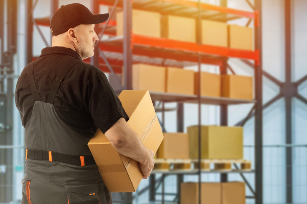 Warehouse worker stands next to warehouse shelving.