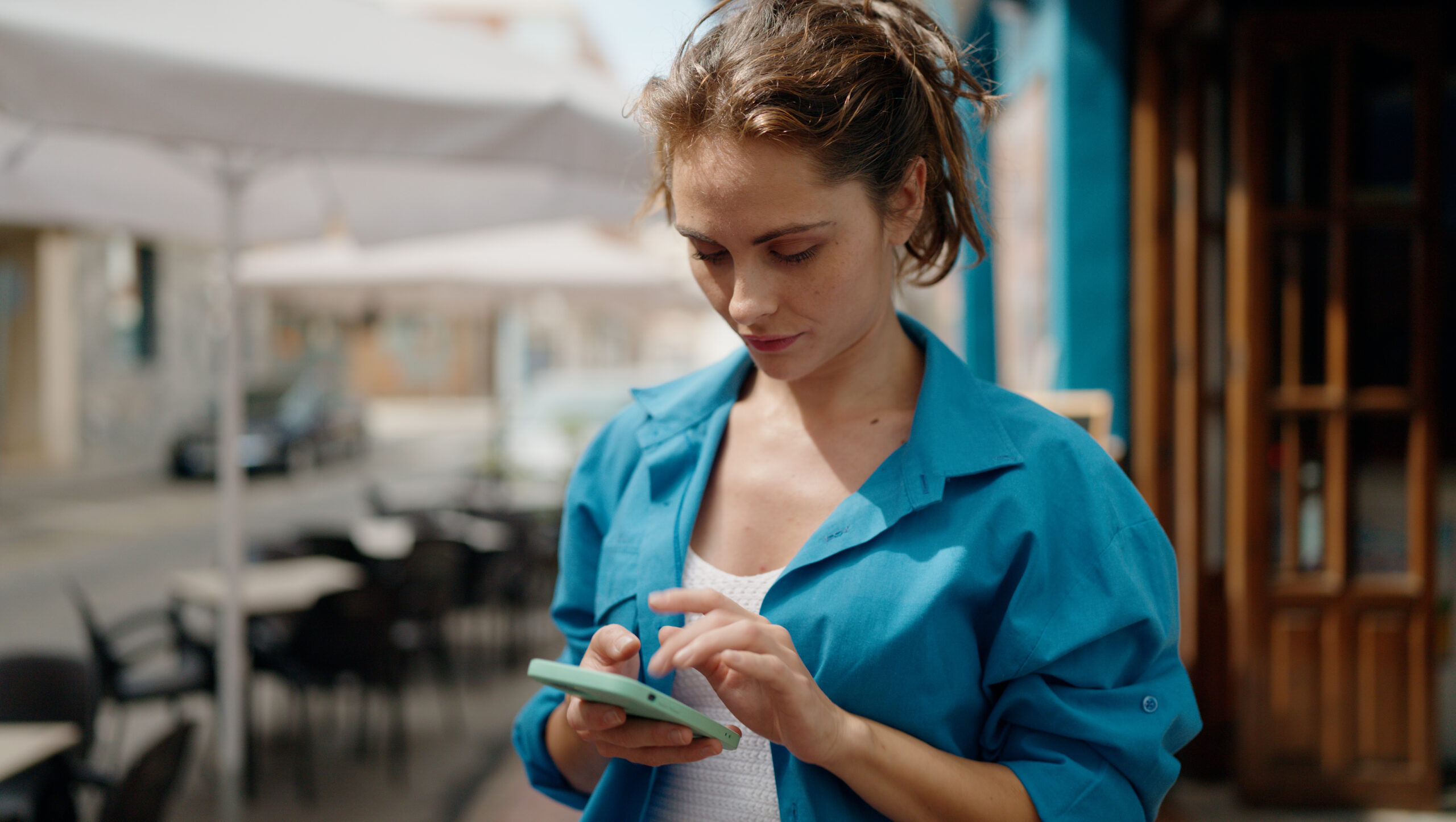 Young woman with serious expression using smartphone at street