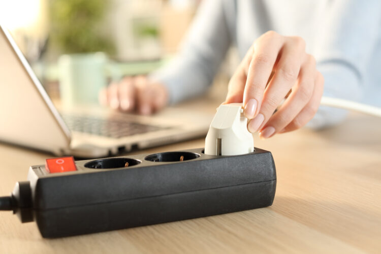 Woman hand plugging laptop to a power socket.