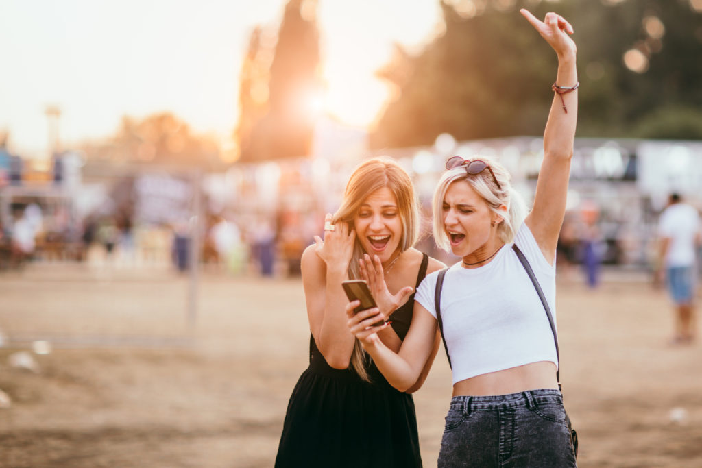 Young female friends having fun and using mobile phone outdoor