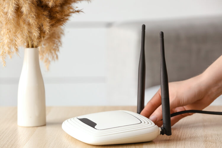 Woman inserting ethernet wire into wi-fi router on table in room