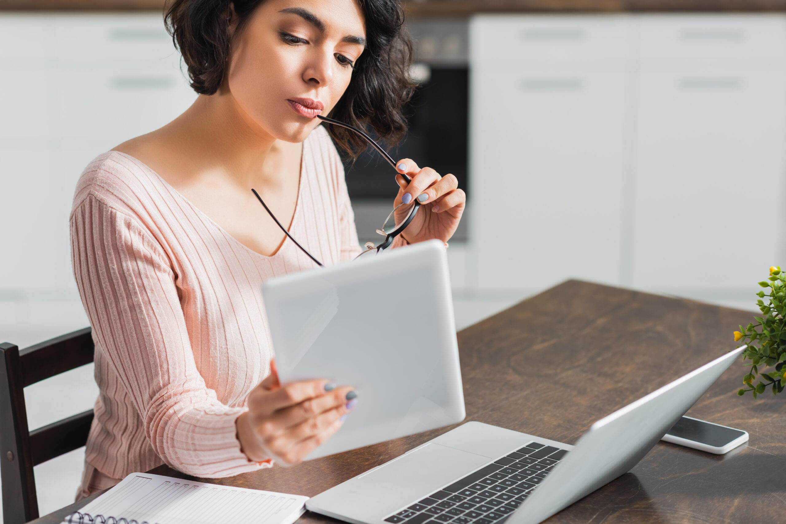 thoughtful woman holding eyeglasses while looking at digital tablet device
