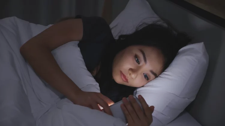 Woman looks worried using phone at night while lying in bed