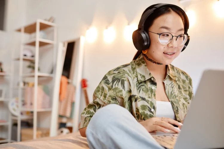 Girl headphones on while using laptop on bed.