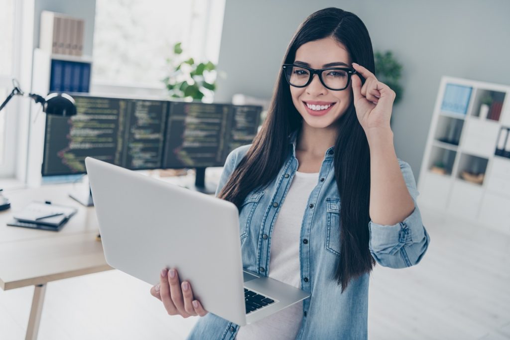 Female employee with glasses holds laptop at office wondering how to get personal files off her work computer.