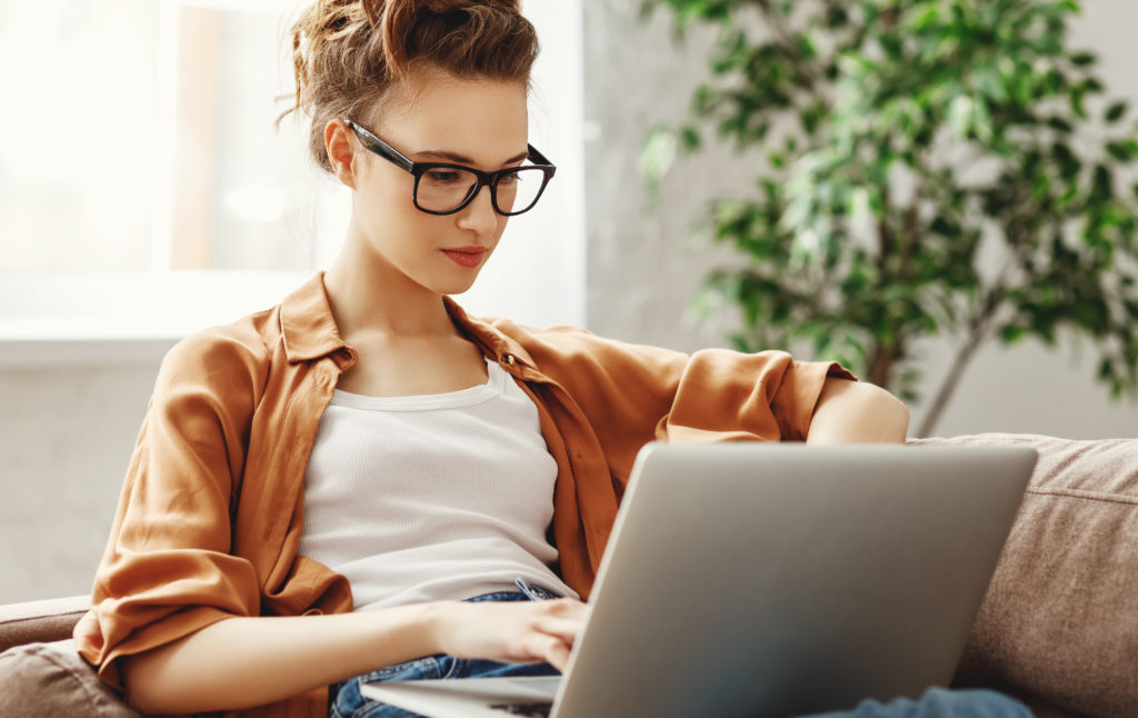 woman with glasses using laptop on sofa