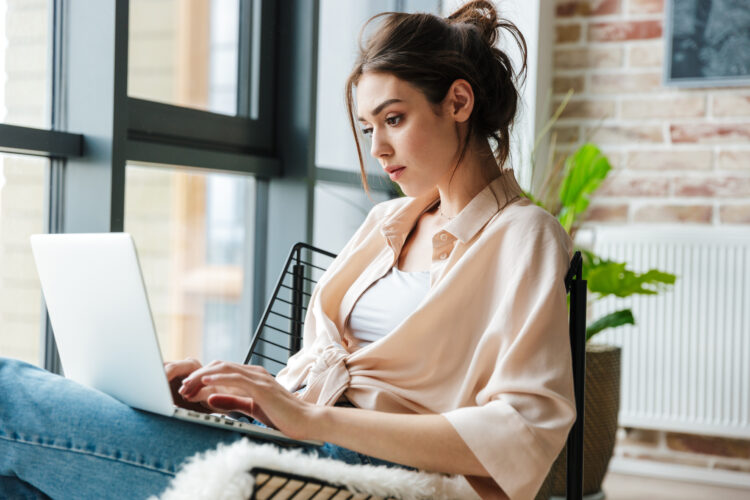 focused woman working with laptop while sitting in armchair