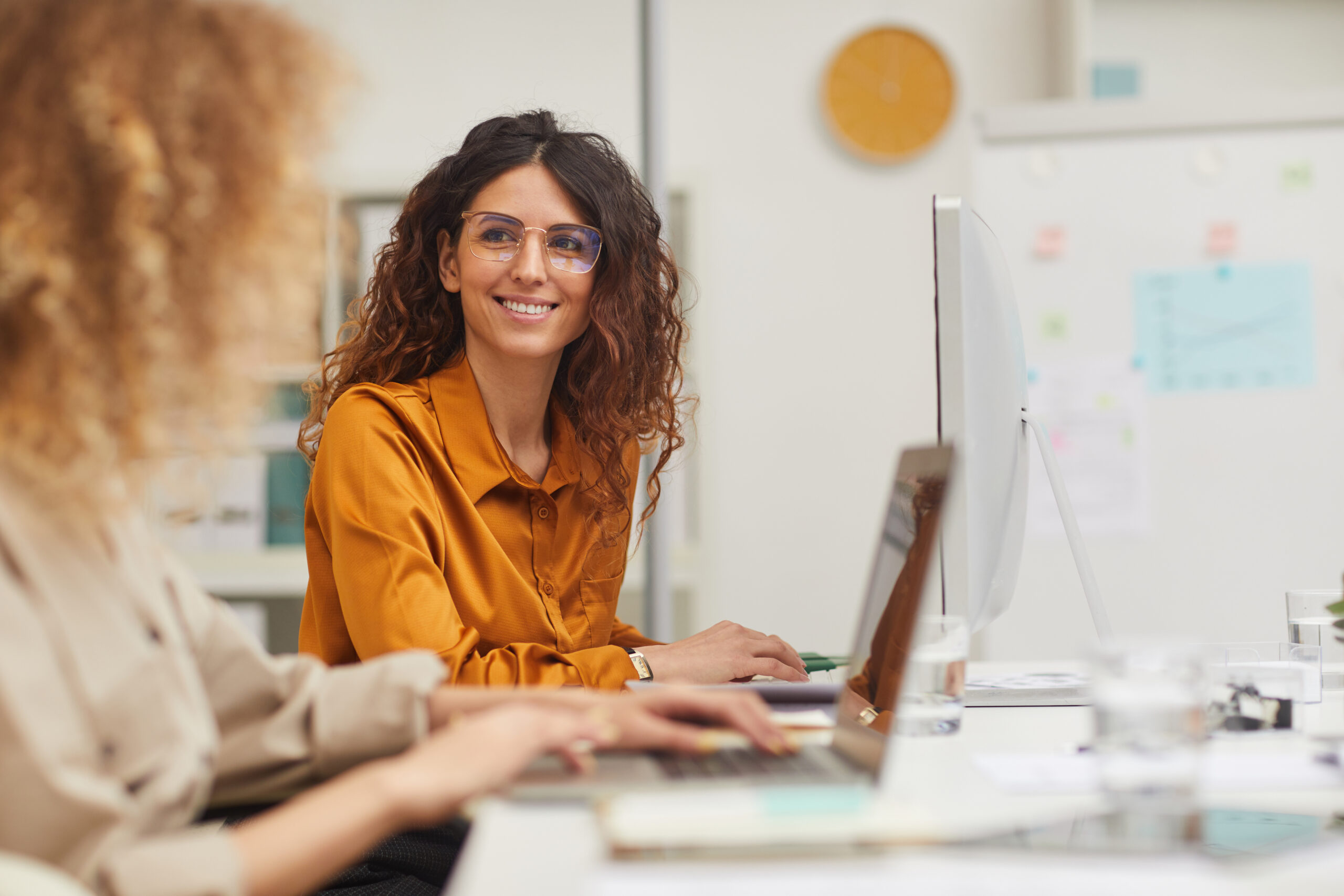 Two charming women interacting with each other while working on their laptops