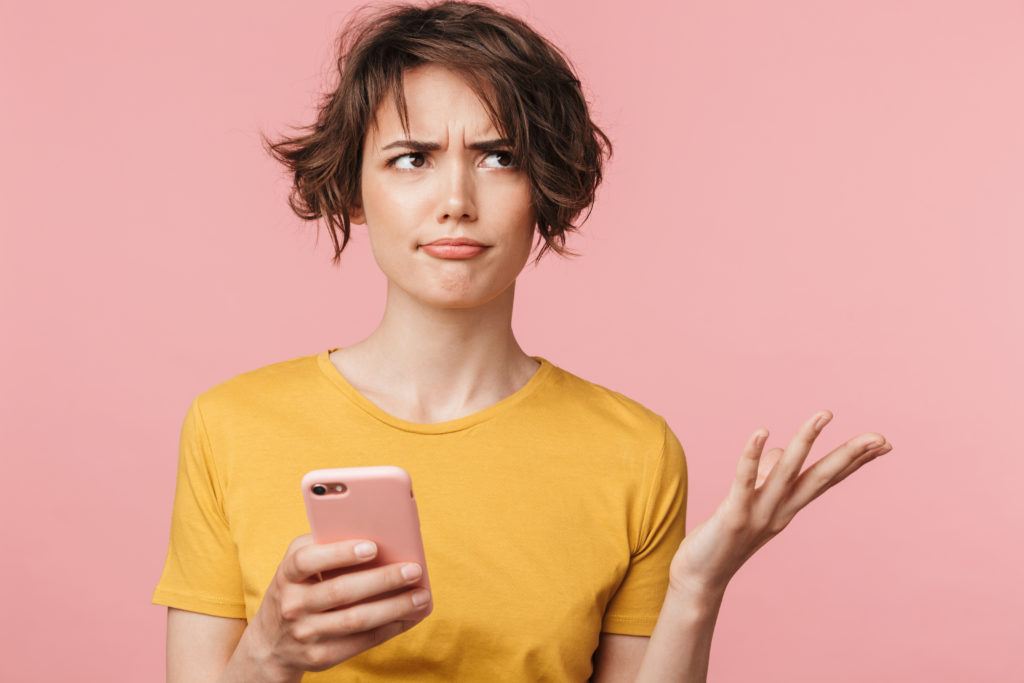 Woman confused with her phone, pink background.