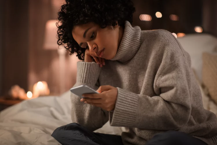 sad-looking woman with smartphone sitting in bed at night