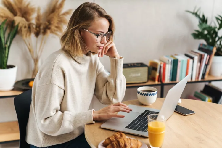 woman using laptop while having breakfast at desk