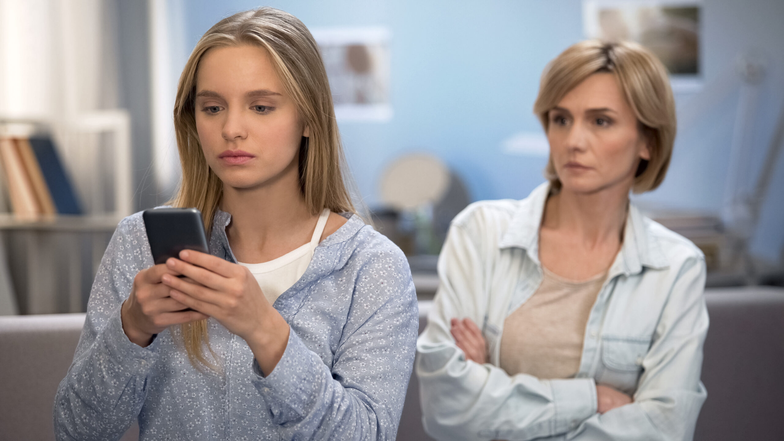 Daughter with smartphone in hands ignoring mom, misunderstanding