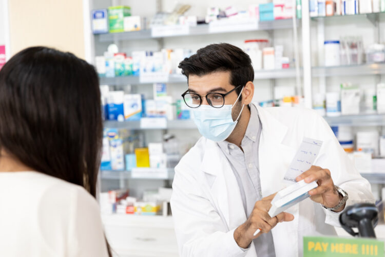 male pharmacist wearing protective hygienic mask questioning woman buying medicines