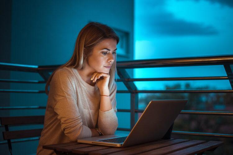 Young beautiful blonde woman working on laptop at night, with nice blue lighting in the background