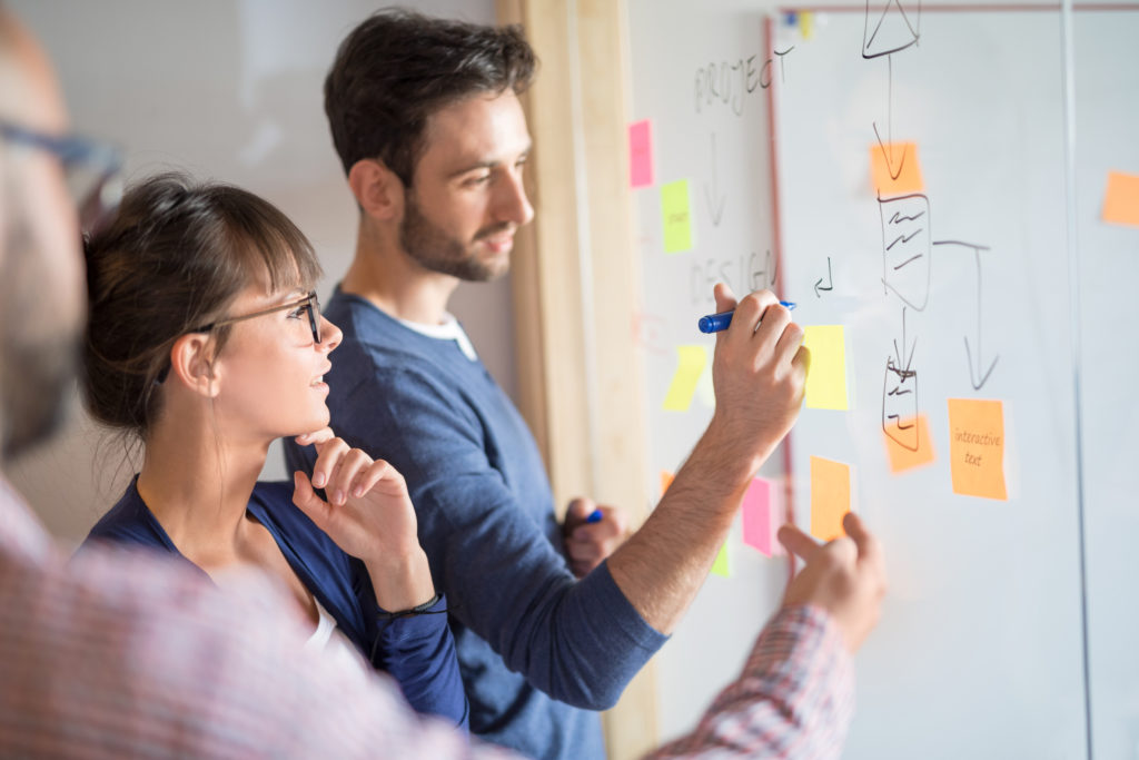 Creative people brainstorming and writing on a transparent board.